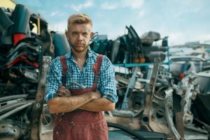 Dirty male repairman on car junkyard