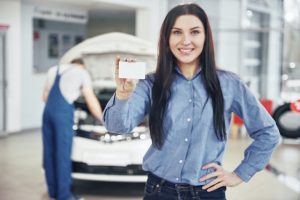 A beautiful woman keeps a business card of the car service center. The mechanic inspects the car